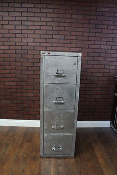 a metal filing cabinet sitting on top of a hard wood floor next to a brick wall