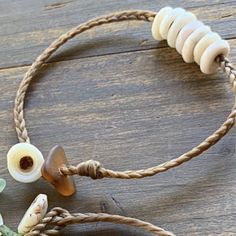 a rope bracelet with seashells and flowers on it sitting on top of a wooden table