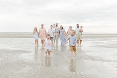 a group of people standing on top of a sandy beach next to the ocean holding hands