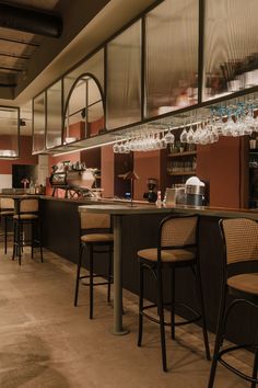 an empty bar with several stools and wine glasses hanging from the ceiling above it