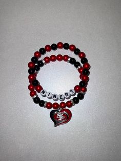 Show off your 49ers pride with this stunning handcrafted bracelet, designed in the team's iconic red and black colors. Made with smooth, high-quality beads, this double-strand bracelet features silver accents and "NINERS" spelled out in bold letters. The centerpiece is a heart-shaped charm with the 49ers logo, perfect for any die-hard fan. Whether you're attending a game or simply adding a touch of your favorite team to your outfit, this bracelet is a stylish and fun accessory for every 49ers supporter! Perfect for gifting or as a personal treat for yourself. Red Team Spirit Bracelets For Gifts, Customized Red Wristband For Friendship, Black Adjustable Beaded Bracelets For Team Spirit, Black Team Spirit Jewelry For Game Day, Personalized Red Bracelets For Team Spirit, Red Personalized Bracelets For Team Spirit, Red Personalized Bracelets With Team Spirit Style, Black Bracelets With Team Spirit For Gift, Adjustable Black Team Spirit Jewelry