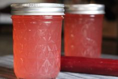 two jars filled with pink liquid sitting on top of a wooden table next to a knife