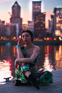 a woman sitting on the edge of a body of water in front of a city skyline