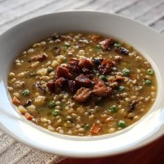 a white bowl filled with soup sitting on top of a wooden table next to a napkin