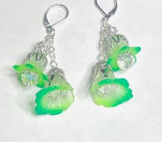 a bold and extraordinary fusion of fluorescent green hues and whimsical fairy vibes. These earrings radiate with vibrant, eye-catching colors, showcasing hand-painted petals that seem to dance with electric energy. Inspired by the captivating glow of fairies, they evoke a sense of wonder and enchantment, making a statement that is both daring and magical. At the heart of these earrings are delicate white flowers, adorned with hand-painted petals in captivating shades of florescent and phthelo green. Each petal is a work of art, showcasing intricate details and a mesmerizing color palette that will catch the eye of everyone around you. Inside each flower, a sparkling clear crystal resides, adding a touch of brilliance and enhancing the overall glamour of the design. The crystals catch the l Whimsical Green Hand Painted Earrings, Whimsical Green Nickel-free Jewelry, Green Fairy Earrings For Gift, Fairy Style Green Earrings For Gifts, Spring Green Flower Earrings With Ear Wire, Spring Green Flower Earrings, Whimsical Green Dangle Earrings, Handmade Green Fairy Jewelry, Green Spring Jewelry With Ear Wire