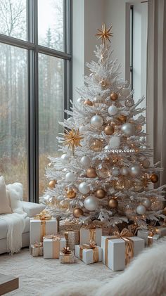 a white christmas tree with gold and silver ornaments in front of a large glass window