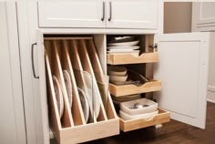 an open cabinet with plates and bowls in the bottom drawer, on a wooden floor