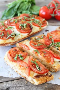 two slices of bread with tomatoes and basil on top, next to some fresh vegetables