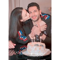 a man and woman are kissing in front of a cake with candles on it while sitting next to each other