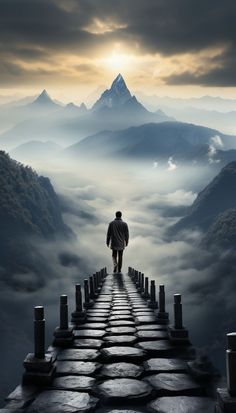 a man walking across a bridge with mountains in the background and foggy sky above