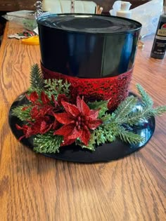 a black top hat with poinsettis and greenery sits on a wooden table