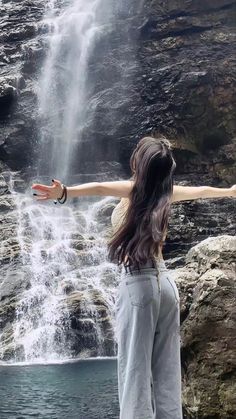 a woman standing in front of a waterfall holding her arms out to the side with both hands