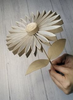 a person holding a paper flower on top of a wooden floor next to a white wall