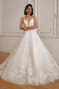 a woman in a white wedding dress standing on a wooden floor with her arms crossed