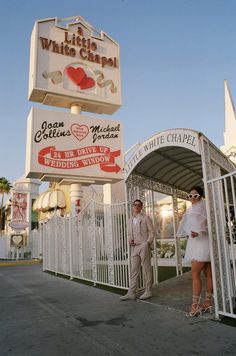 a man and woman standing in front of a white chapel with red hearts on it