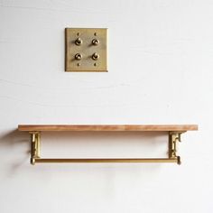 two brass brackets on the wall above a wooden shelf