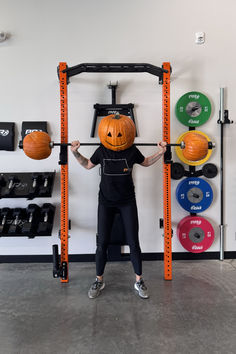 a person wearing a pumpkin mask while holding a barbell and weight scale in front of their face