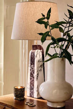 a white vase sitting on top of a table next to a lamp and a candle