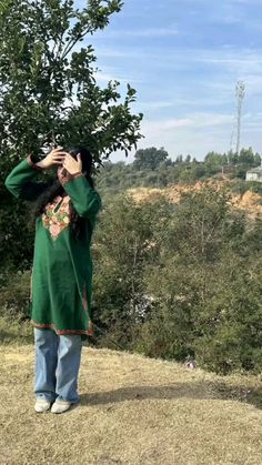 a woman standing on top of a grass covered hillside looking through binoculars at the sky