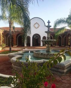 a fountain in the middle of a courtyard surrounded by palm trees and other greenery