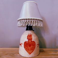 a table lamp with a red heart painted on the base and fringed lampshade