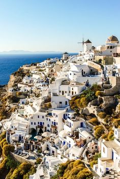 white buildings on the side of a cliff by the ocean with blue water in the background