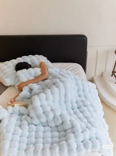 a woman laying on top of a bed under a fluffy blue blanket with clouds in it