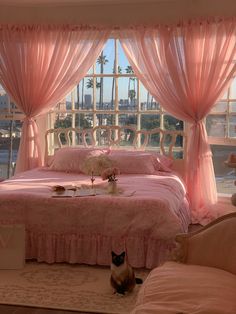 a cat sitting on the floor in front of a bed with pink sheets and drapes