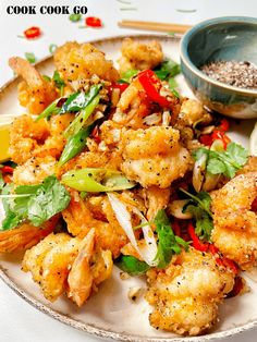 a white plate topped with shrimp and veggies next to a bowl of seasoning