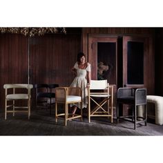 a woman in a dress standing at a table with chairs and a chair next to her