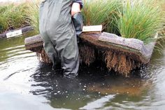 a man standing in the water next to a bench made out of mud and grass