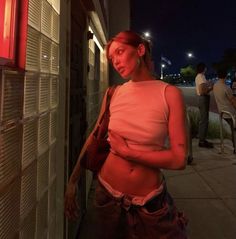 a woman standing next to a building with her stomach exposed and no shirt on at night