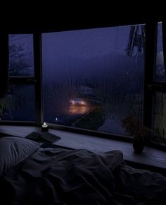 a bed sitting under a window next to a night time sky filled with raindrops