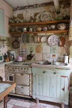 an old fashioned kitchen with lots of dishes on the wall and cupboards over the stove