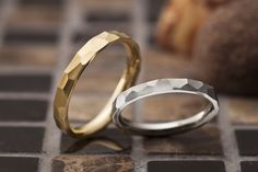 two gold and silver wedding bands sitting on top of a tiled floor next to each other