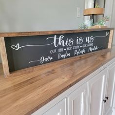 this is us sign sitting on top of a wooden counter in a kitchen with white cabinets