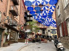 several blue umbrellas hanging from the ceiling in an alleyway with people sitting at tables