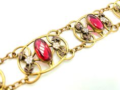 "This lovely bracelet features oval bezel set rhinestones in a deep ruby red color. The stones are flanked by white enamel flowers with red leaves that coordinate with the stones. These stones and enamel are all set in antique brass links. This wide, delicate bracelet has all the hallmarks of a Neiger piece (although these were not signed, so it's a bit hard to be sure). In any event, this is a prime example of Art Deco Czech jewelry. CONDITION/SIZE: Excellent vintage condition. About 7.5\" long Czech Jewelry, Red Rhinestone, Enamel Flower, Rhinestone Bracelet, Vintage Bracelets, Art Deco Jewelry, White Enamel, Bezel Setting, Vintage Art Deco