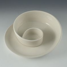 two white bowls and saucers sitting on top of each other in front of a gray background