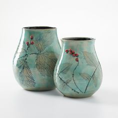 two vases with leaves and berries painted on the sides, one is green and the other is blue