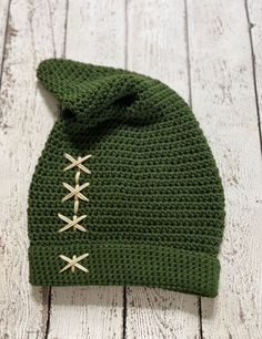 a green knitted hat with gold pins on the front and side, sitting on a white wooden surface