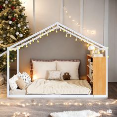 a dollhouse bed with lights on it and a christmas tree in the background