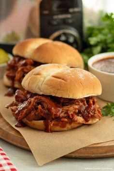 two pulled pork sandwiches sitting on top of a cutting board next to a bowl of salsa