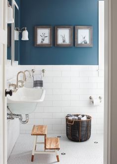 a bathroom with blue walls and pictures on the wall above the sink, along with a wooden step stool