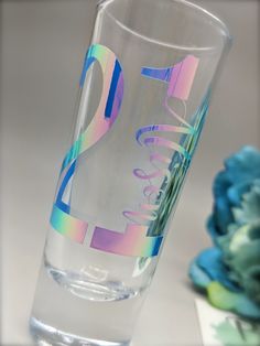 a clear glass with the number twenty five on it next to blue flowers and a vase