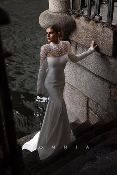 a woman in a long white dress standing on some steps next to water and looking off into the distance