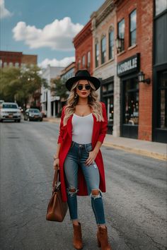 a woman standing on the street wearing ripped jeans and a red cardigan coat with a black hat