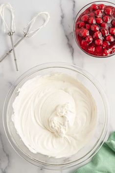 two bowls filled with whipped cream and cherries on top of a marble countertop