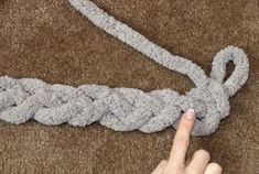 a hand pointing at a crochet knot on the floor