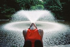 a woman sitting in front of a fountain with water shooting up into the air from her back